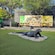 A Komodo dragon statue on the grass near a wall with a world map, animal pictures and 2 picnic tables